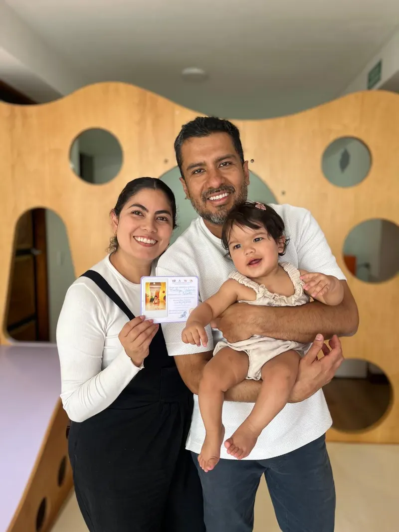 Mamá y papá sosteniendo a su bebé y su diploma, frente al muro ondulado