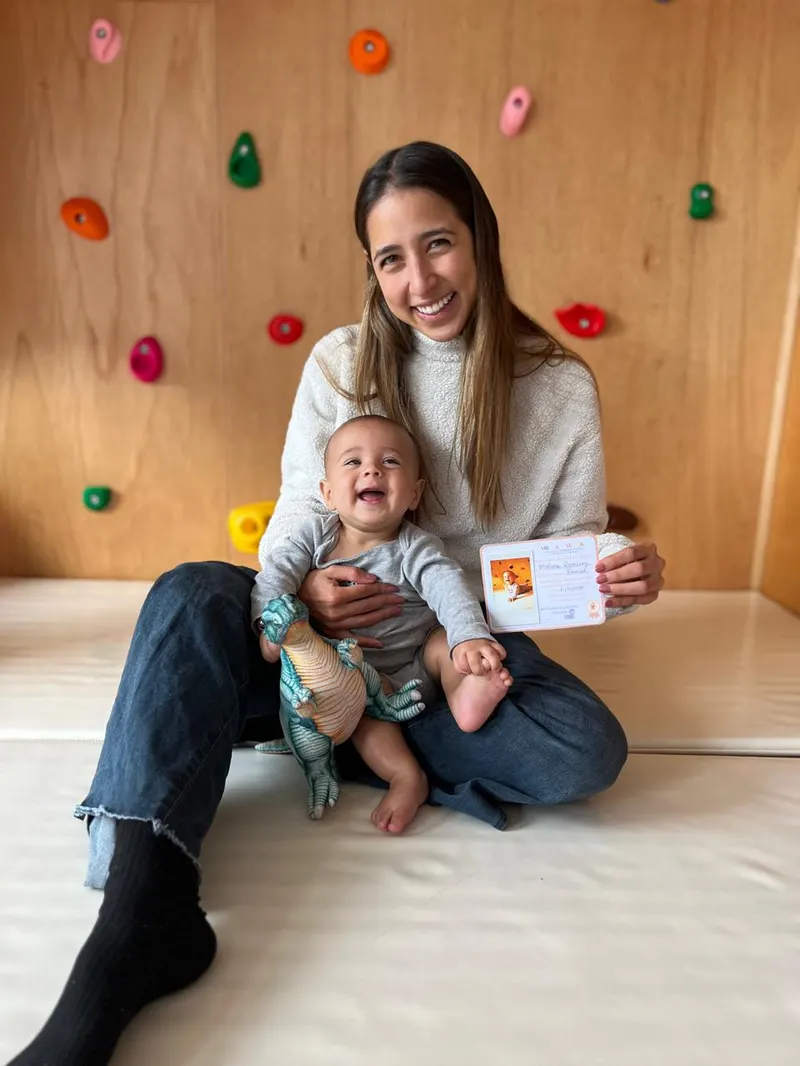 Mamá abrazando a su bebé, que sostiene un dinosaurio de peluche