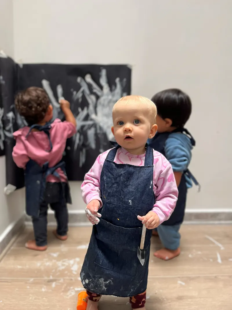 Tres niños con delantal pintando juntos, de pie frente a un mural