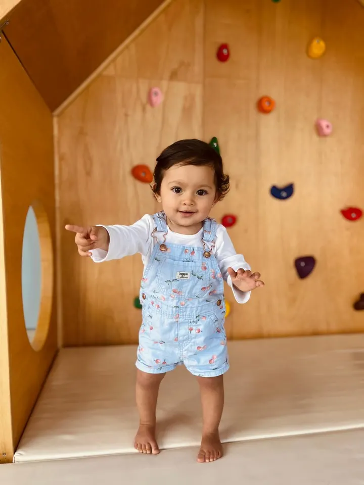 Niña de pie señalando, frente al muro de escalada de Wawa